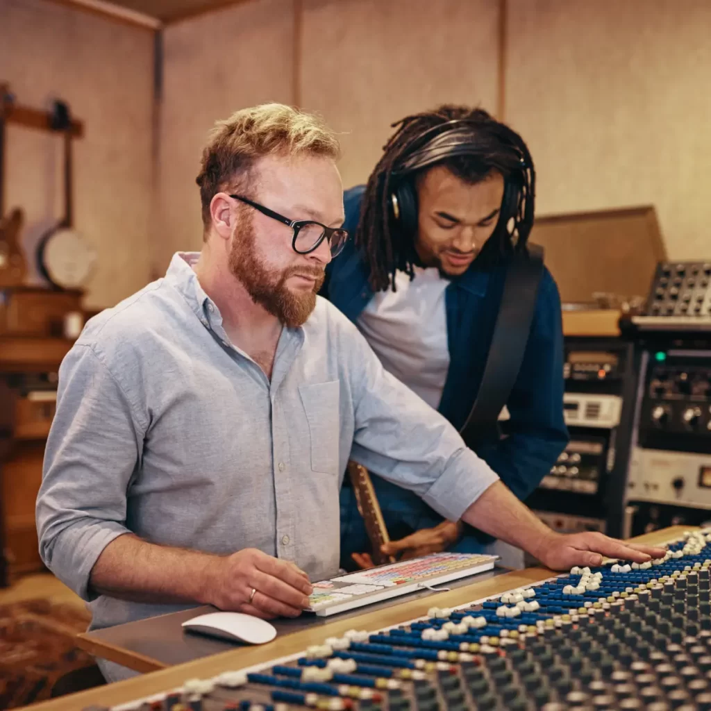 Music producer and guitarist reviewing audio levels at a mixing console in a recording studio.