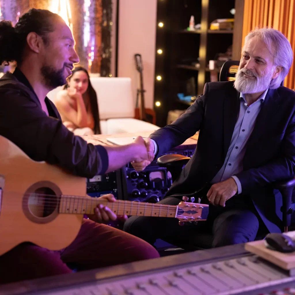 Musician with a guitar shakes hands with a producer in a recording studio.