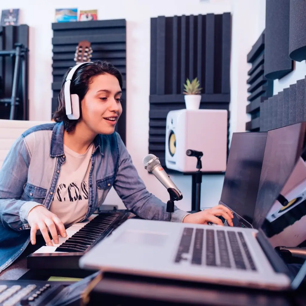 Musician wearing headphones and working on a keyboard and laptop in a soundproofed home studio.