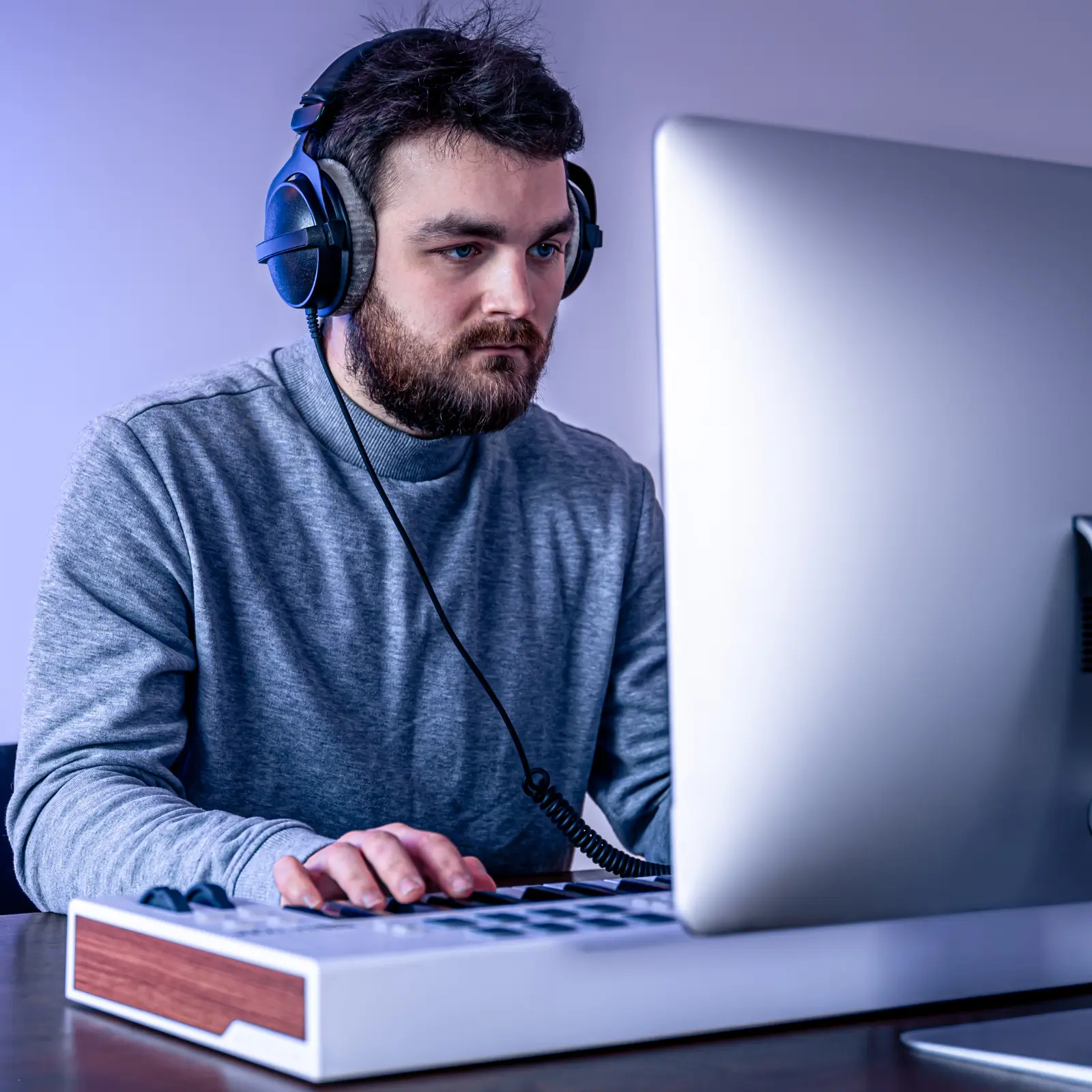 Independent music publishing setup with man wearing headphones working on a computer in a home studio.