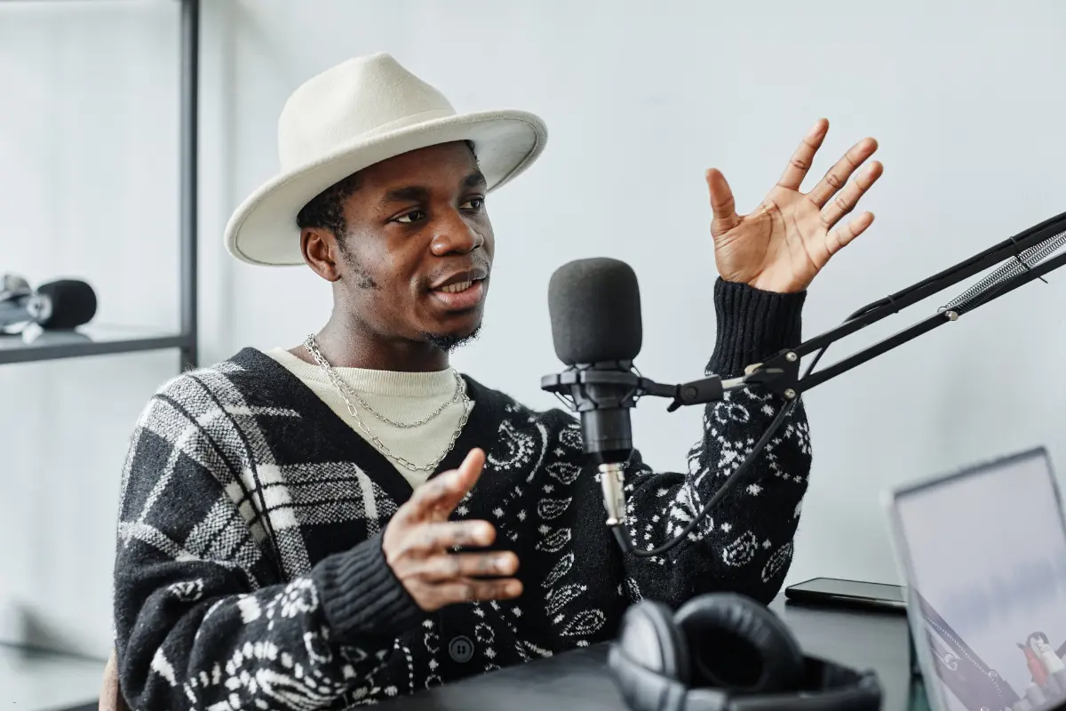 A podcaster wearing a stylish hat and sweater, passionately speaking into a microphone about Spotify playlist placement.