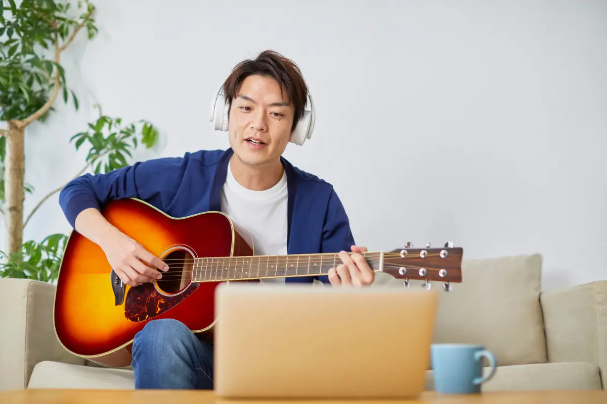 A young artist wearing headphones, playing guitar while engaging in Spotify promotion for artists via an online platform.