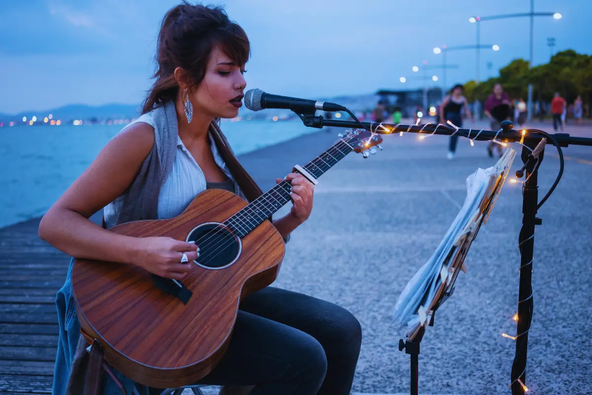 Get discovered by A&R teams by performing live, as shown by this musician singing and playing guitar on a waterfront stage