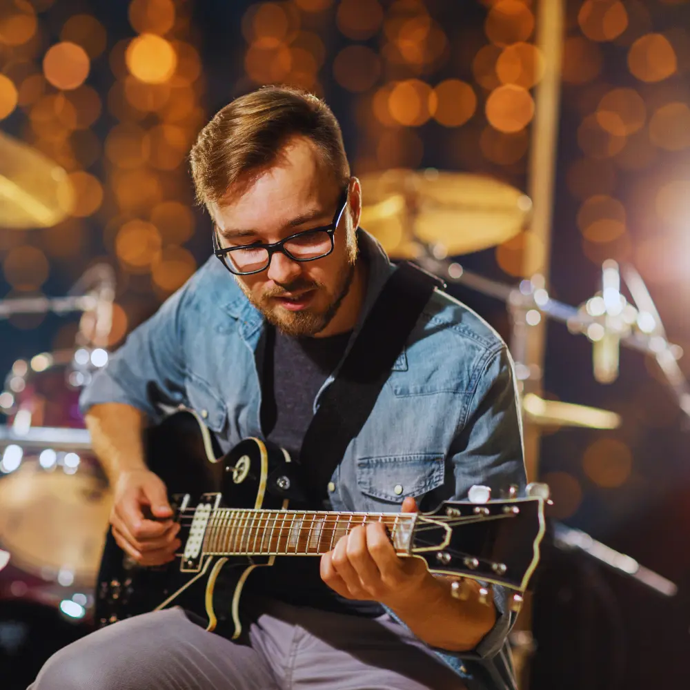 A guitarist in glasses plays an electric guitar on stage, showcasing ways to monetize music rights.