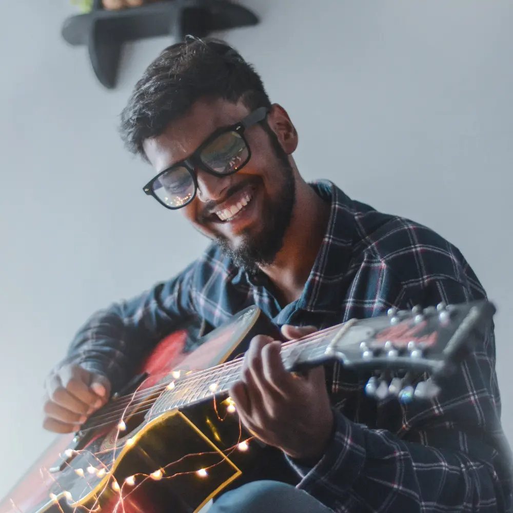 Music PR for EP launch involves strong visuals, like this smiling musician playing an acoustic guitar with fairy lights.