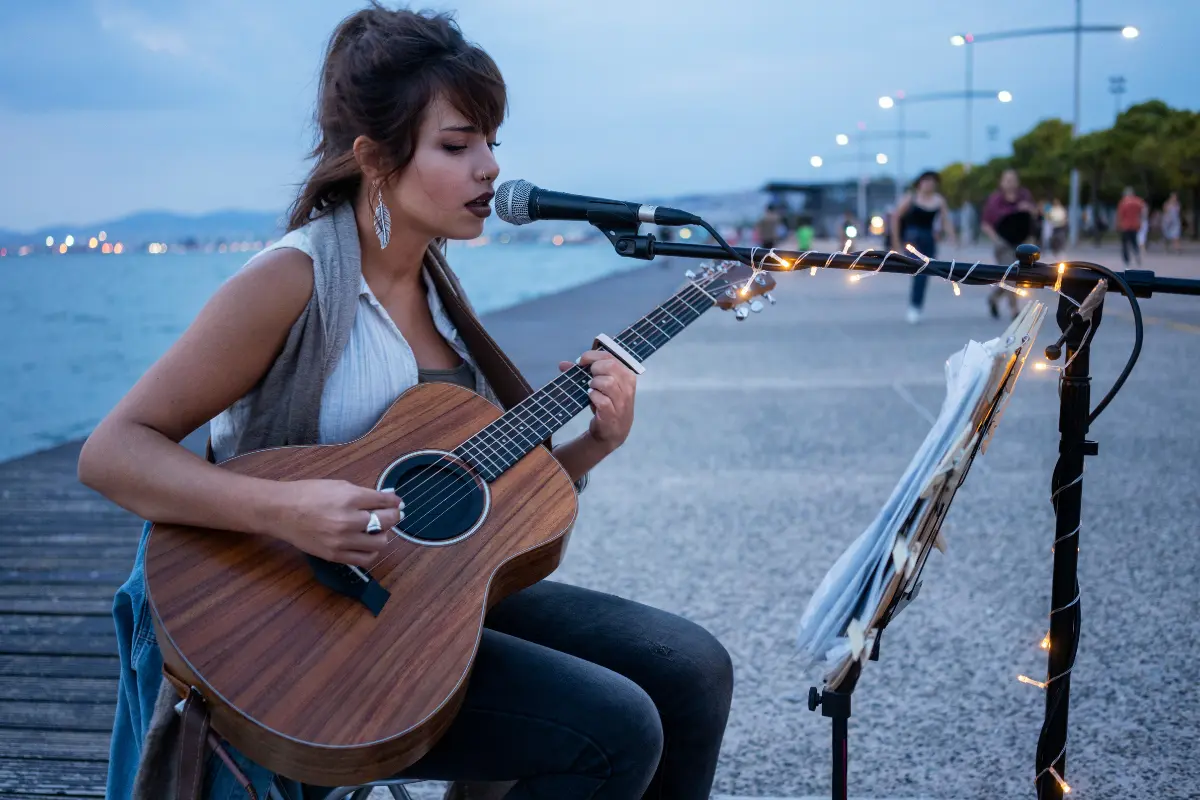 A female musician performing with a guitar by the waterfront, showcasing the power of live music marketing.