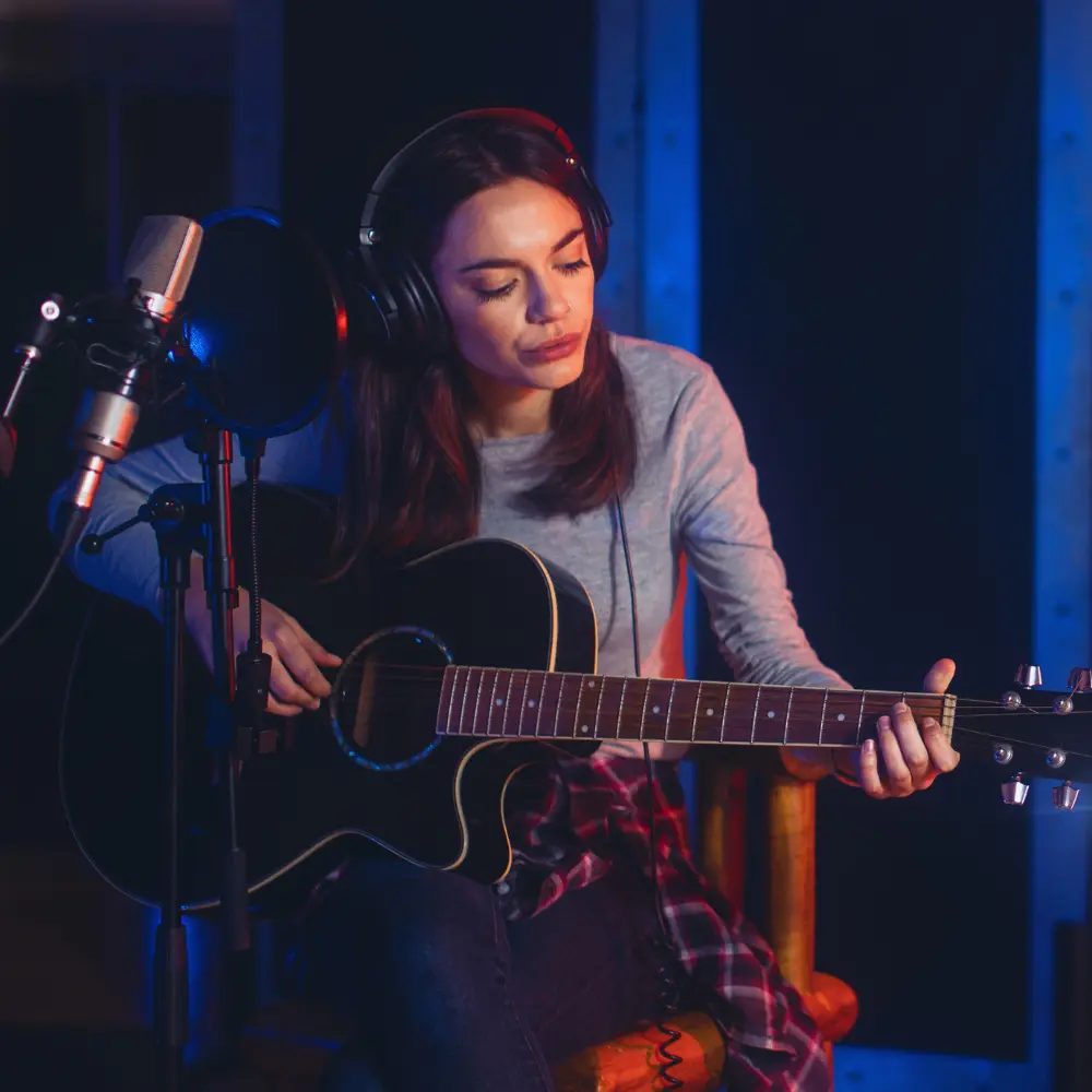 music sync licensing strategies showcased with a singer-songwriter playing an acoustic guitar while recording vocals.