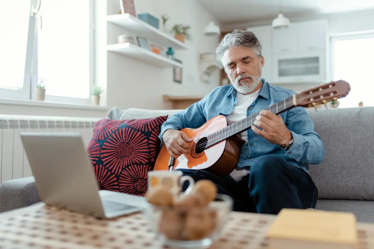 A man playing an acoustic guitar on a couch while watching an online lesson to promote music on Spotify.