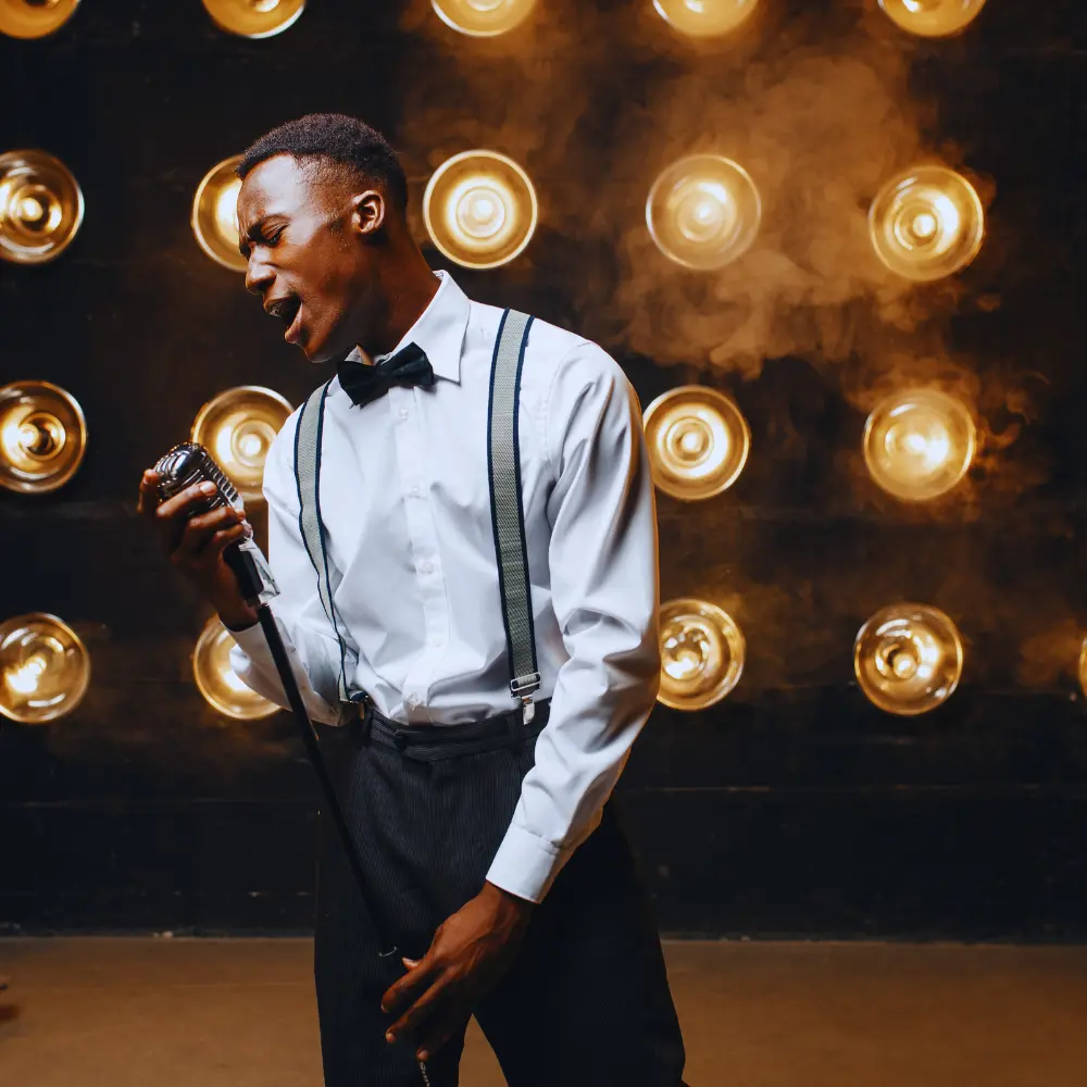 A stylish male vocalist in suspenders sings into a vintage microphone under dramatic stage lighting, illustrating sync representation.