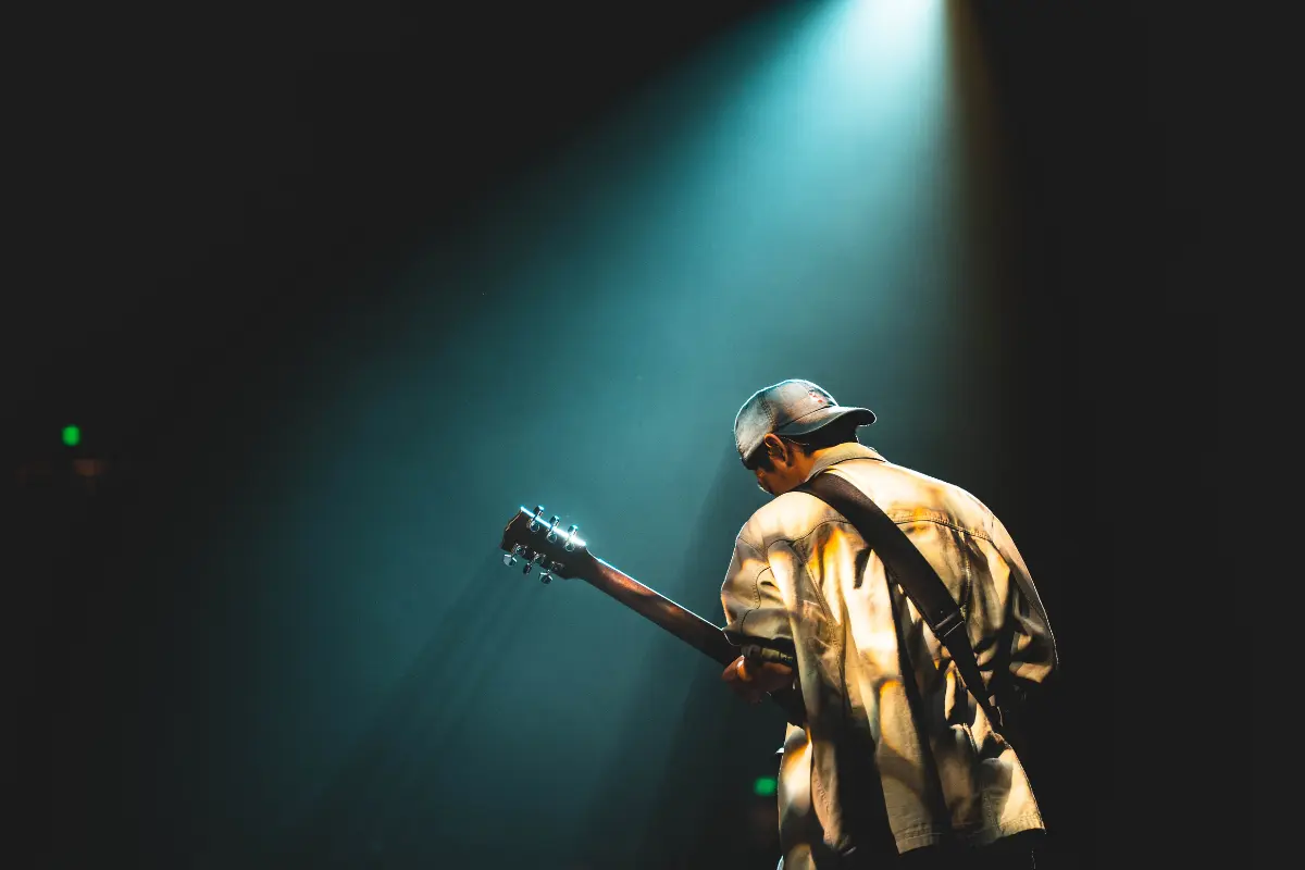 Music royalties for indie artists shown through a solo guitarist performing under a focused stage spotlight